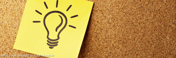 Ein gelber Zettel mit einer gezeichneten leuchtenden Glühbirne auf einer Korktafel