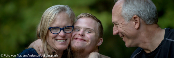 Foto von einer behinderten Person, die von einer Frau und einem Mann umarmt wird